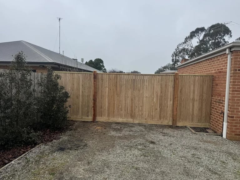 Wooden privacy fence enclosing a gravel courtyard between brick houses on a suburban property