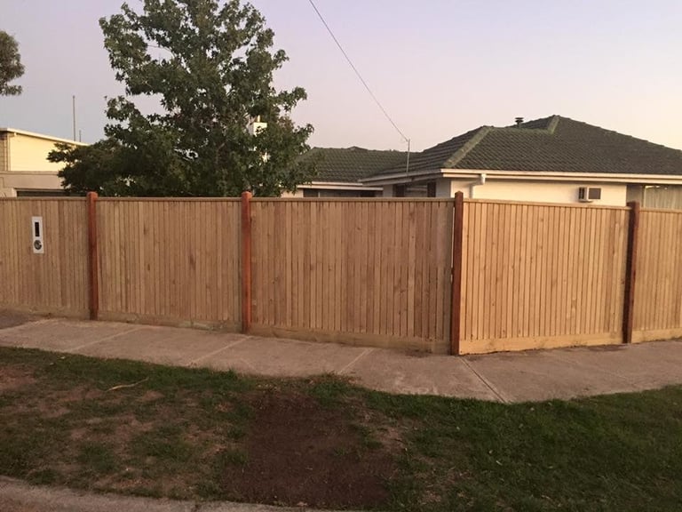 Tan metal corrugated fence with red posts surrounding a residential backyard at dusk, with houses visible in background