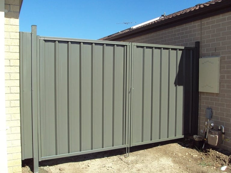Double sliding metal gate with corrugated iron panels attached to a brick wall in a residential yard