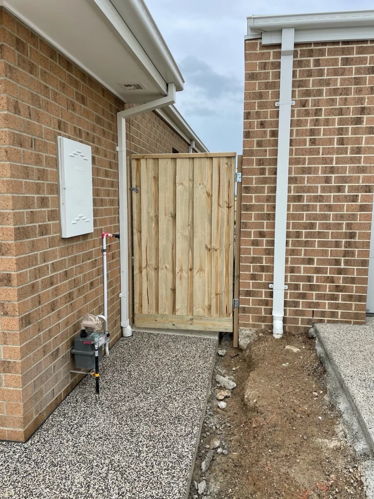 Wooden gate entrance between brick buildings with gravel and soil ground areas