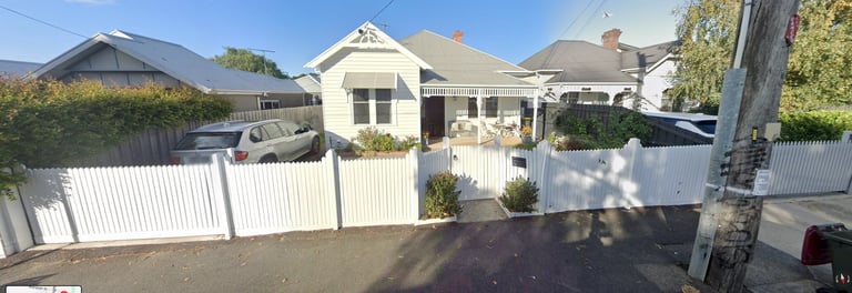 White cottage-style house with white fence and driveway on a sunny day