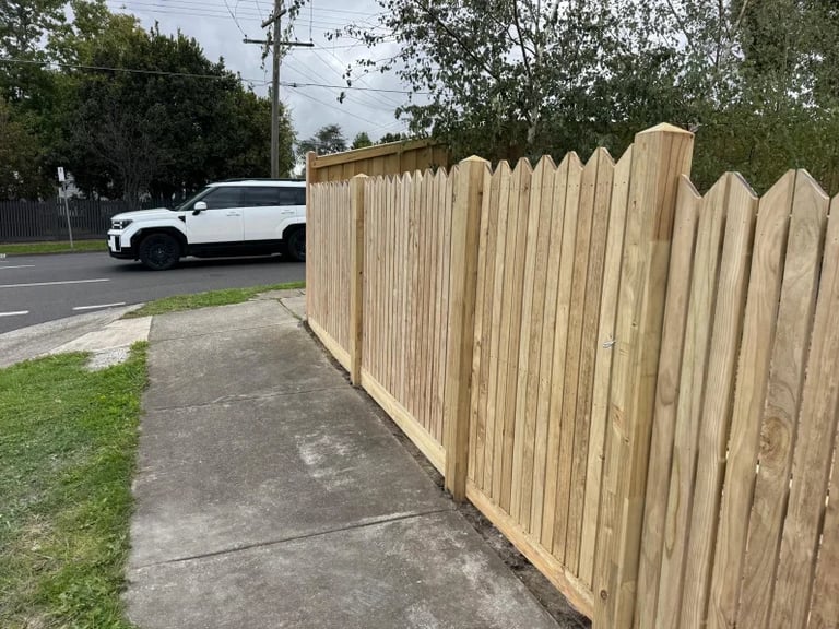Wooden fence along a sidewalk with a white SUV parked on the street behind it