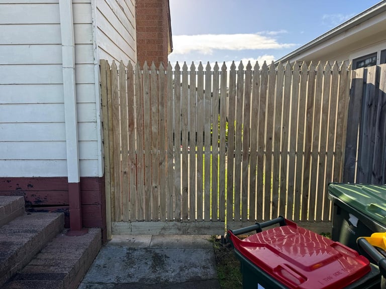 Weathered wooden picket fence in backyard with red kayak and green storage box in foreground