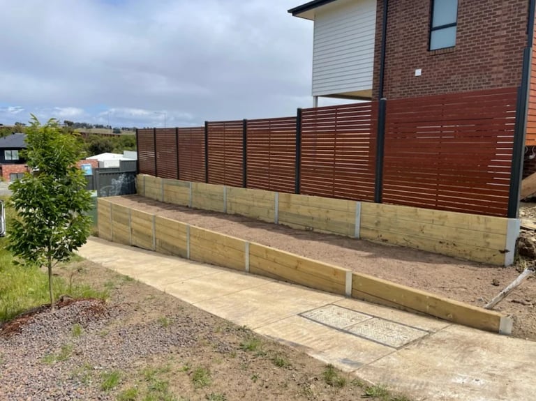 Residential property with brown slatted fencing and wooden retaining walls bordering a paved patio area